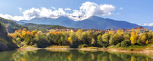 Bansko, Bulgaria Autumn Banner Panorama Background Of Pirin Mountain Peaks, Krinets Lake Water, Colorful Green, Red And Yellow Trees Reflection
