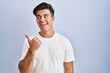 © Krakenimages.com - Hispanic man standing over blue background smiling with happy face looking and pointing to the side with thumb up.