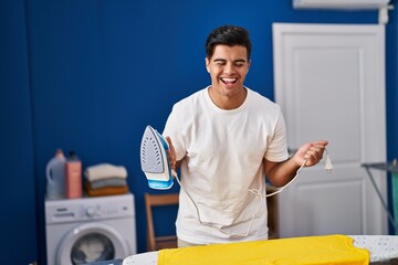 Canvas Print - Hispanic man holding electric iron smiling and laughing hard out loud because funny crazy joke.