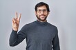 © Krakenimages.com - Handsome latin man standing over isolated background smiling looking to the camera showing fingers doing victory sign. number two.