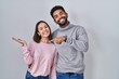 © Krakenimages.com - Young hispanic couple standing together amazed and smiling to the camera while presenting with hand and pointing with finger.
