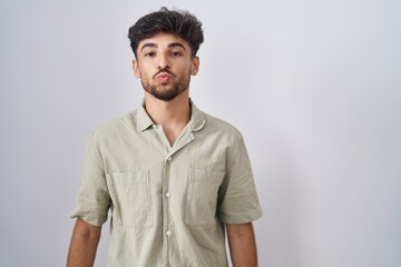 Wall Mural - Arab man with beard standing over white background looking at the camera blowing a kiss on air being lovely and sexy. love expression.