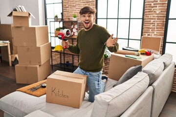 Canvas Print - Arab man with beard moving to a new home closing cardboard box celebrating achievement with happy smile and winner expression with raised hand