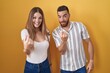 © Krakenimages.com - Young couple standing over yellow background beckoning come here gesture with hand inviting welcoming happy and smiling