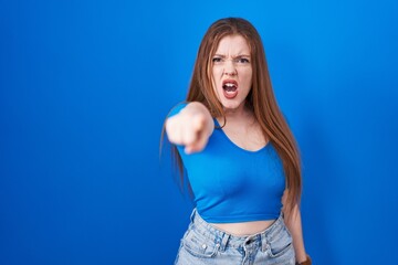 Canvas Print - Redhead woman standing over blue background pointing displeased and frustrated to the camera, angry and furious with you