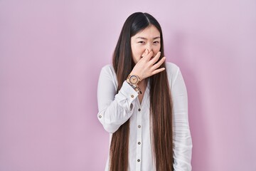 Sticker - Chinese young woman standing over pink background smelling something stinky and disgusting, intolerable smell, holding breath with fingers on nose. bad smell