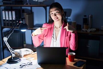 Wall Mural - Chinese young woman working at the office at night looking confident with smile on face, pointing oneself with fingers proud and happy.