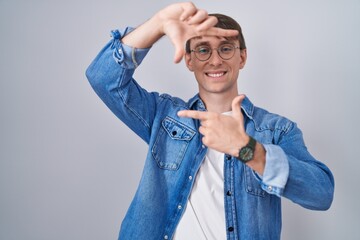 Poster - Caucasian blond man standing wearing glasses smiling making frame with hands and fingers with happy face. creativity and photography concept.