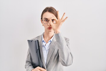 Canvas Print - Young caucasian woman wearing business clothes and glasses doing ok gesture shocked with surprised face, eye looking through fingers. unbelieving expression.