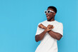© Богдан Маліцький - african american man in white t-shirt and sunglasses dances to music and sings on blue isolated background