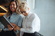 © Jacob Lund - Two business women laugh happily as they use a digital tablet together in a modern office