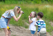 Mother With Two Little Children Boy And Girl Examining Plants And Trees Through Magnifying Glass And Binocular While Exploring Forest Nature And Environment On Sunny Day During Outdoor Ecology