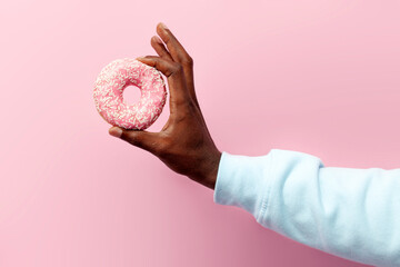 african man's hand holds sweet round donut on pink isolated background, the guy's hand advertises fast food