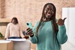 African woman using smartphone at new home pointing thumb up to the side smiling happy with open mouth