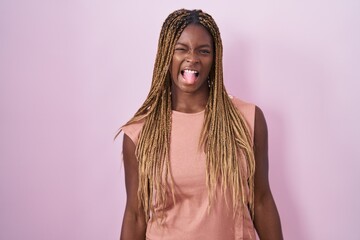 Wall Mural - African american woman with braided hair standing over pink background sticking tongue out happy with funny expression. emotion concept.