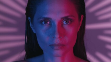 Close up shot of an attractive young woman's face turned at the camera with a concentrated and serious look in a neon pink and blue light.