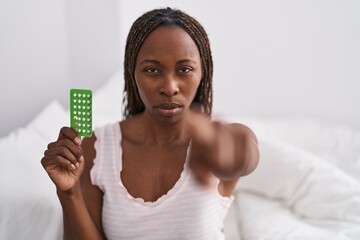 Poster - African american woman holding birth control pills pointing with finger to the camera and to you, confident gesture looking serious