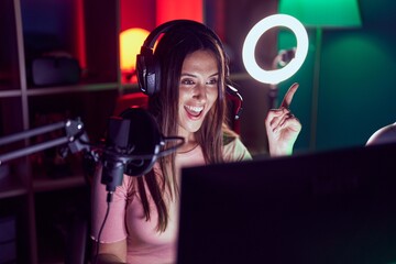 Poster - Young brunette woman playing video games smiling happy pointing with hand and finger to the side