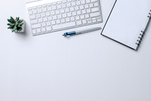 Top View Of Keyboard Computer, Notebook, Pen And Succulent On White Desk With Blank Space For Text Or Ads