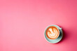 A cup of cappuccino with latte art on pink background. Top view with copyspace for your text.  A morning drink sitting on top of a table. 