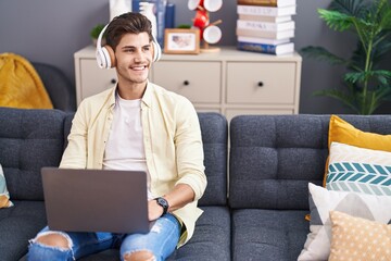 Wall Mural - Young hispanic man listening to music sitting on sofa at home