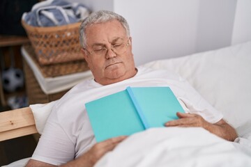 Poster - Middle age grey-haired man lying on bed sleeping holding book at bedroom