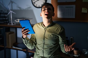 Wall Mural - Non binary person using touchpad device at night angry and mad screaming frustrated and furious, shouting with anger. rage and aggressive concept.