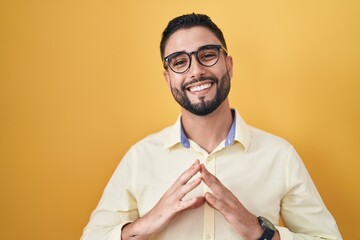 Canvas Print - Hispanic young man wearing business clothes and glasses hands together and fingers crossed smiling relaxed and cheerful. success and optimistic