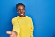 © Krakenimages.com - Beautiful black woman standing over blue background smiling friendly offering handshake as greeting and welcoming. successful business.