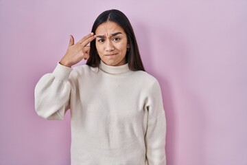 Wall Mural - Young south asian woman standing over pink background shooting and killing oneself pointing hand and fingers to head like gun, suicide gesture.
