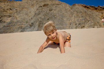 Wall Mural - Happy children, boys, playing on the beach on sunset, kid cover in sand, smiling, laughing