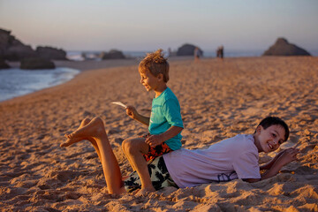 Canvas Print - Child, tickling sibling on the beach on the feet with feather, kid cover in sand, smiling, laughing