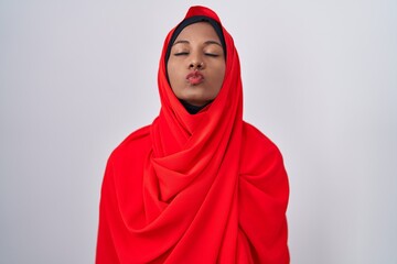 Wall Mural - Young arab woman wearing traditional islamic hijab scarf looking at the camera blowing a kiss on air being lovely and sexy. love expression.