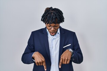 Poster - Young african man with dreadlocks wearing business jacket over white background pointing down with fingers showing advertisement, surprised face and open mouth