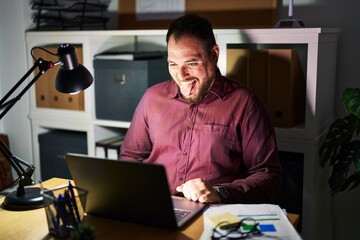 Canvas Print - Plus size hispanic man with beard working at the office at night sticking tongue out happy with funny expression. emotion concept.