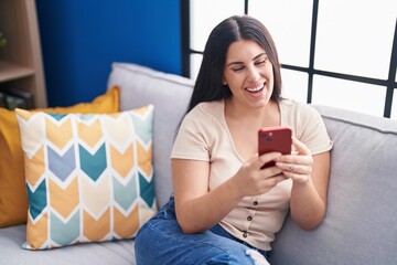 Canvas Print - Young beautiful hispanic woman using smartphone sitting on sofa at home