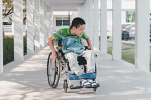 Asian Child With A Blue Backpack Smiling Face With Happiness Wheelchair Pushed By Himself On The Ramp Of Home Or Hospital,school,nursery,concept Of Facilities Necessary For People With Disabilities.