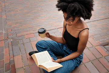 Black woman is reading a book sitting on floor.