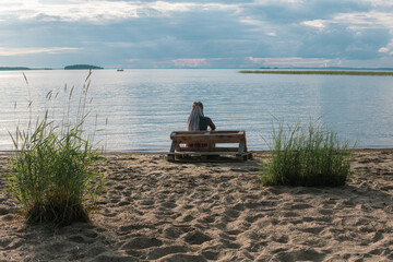 Wall Mural - woman traveler with de braids hairstyle sitting on a sandy shore of a vast lake