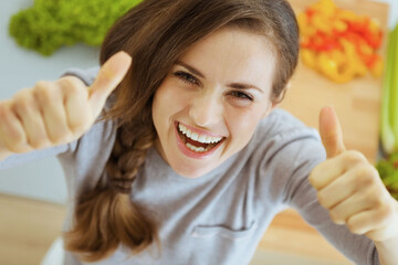 Wall Mural - Happy young housewife in modern kitchen showing thumbs up