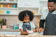 © chokniti - Kind African american parents teaching their adorable daughter how to cook healthy food, free space of kitchen, Happy black people family preparing healthy food in kitchen together