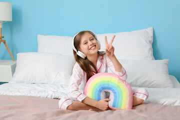 Sticker - Little girl with headphones and rainbow pillow showing victory gesture in bedroom