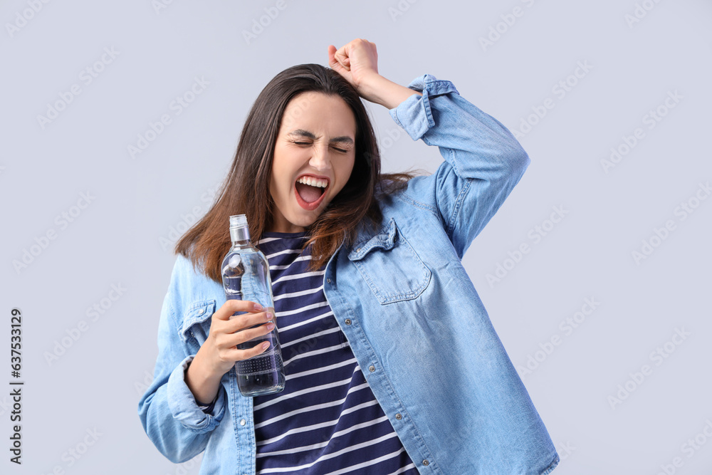 Young woman with bottle of vodka on light background