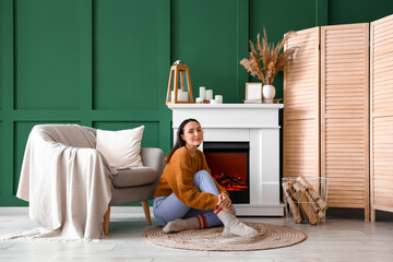 Young woman sitting near fireplace at home