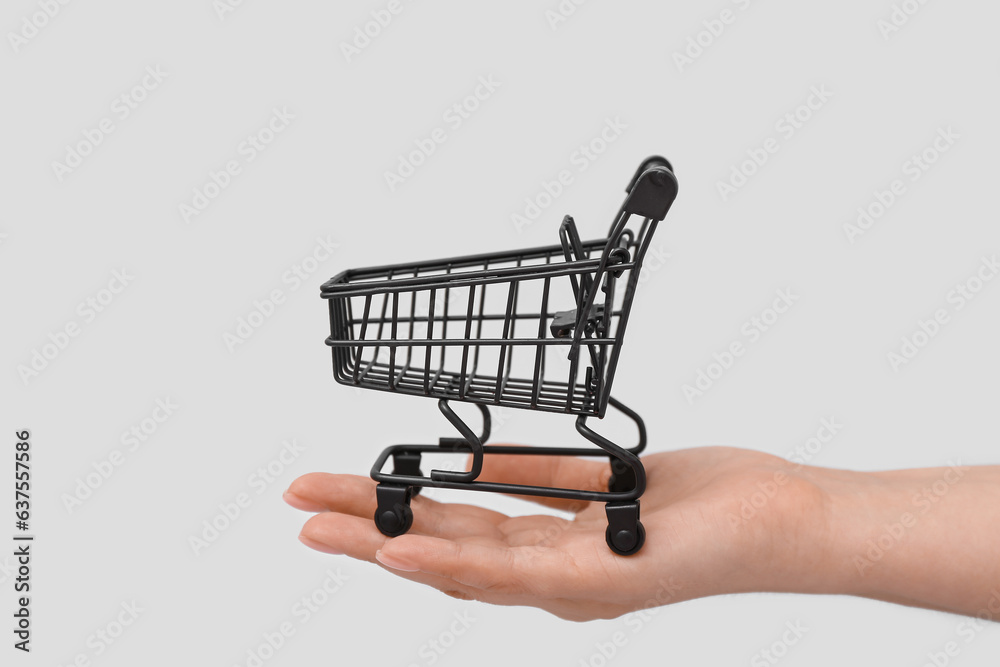 Female hand with shopping cart on grey background