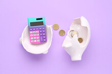 Broken Piggy Bank With Calculator And Coins On Lilac Background