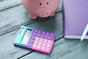 Calculator, piggy bank and notebook on blue wooden background