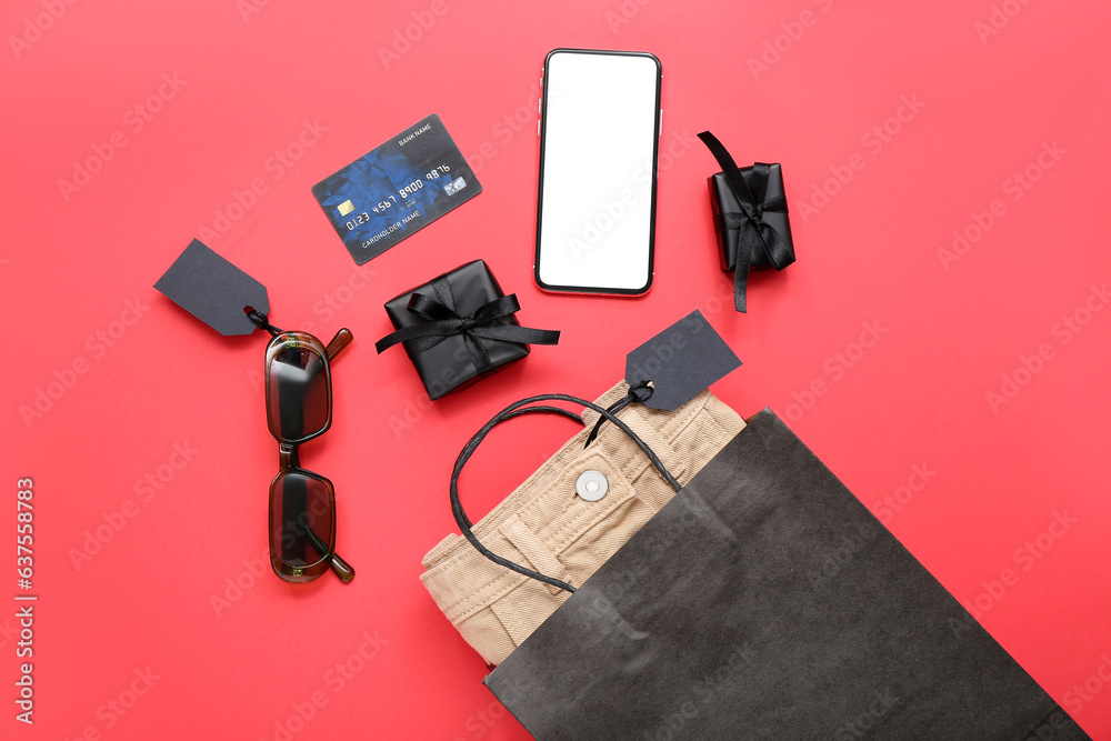 Shopping bag with pants, sunglasses and gift boxes on red background. Black Friday concept