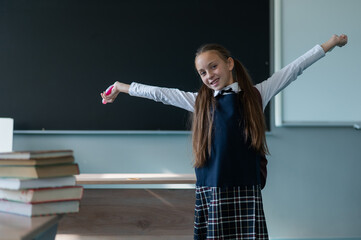 Wall Mural - A caucasian girl stands with her arms outstretched at the blackboard. The lessons are over.