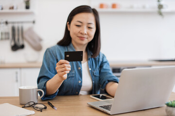 Lady staring at debit card while surfing net on laptop